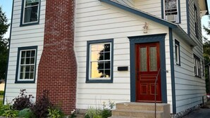 A two-story house with a red door, a brick chimney, and a small front porch. - Charming 3-bedroom house in Gouverneur with private basketball court. (Gouverneur)
