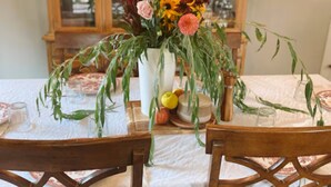 A dining table set with chairs, a floral centerpiece, and a wooden cabinet in the background. - Charming 3-bedroom house in Gouverneur with private basketball court. (Gouverneur)