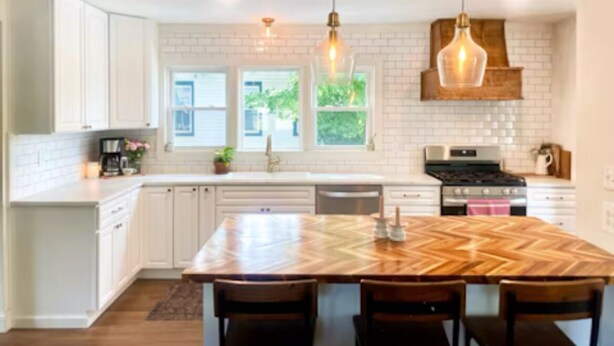 A modern kitchen with white cabinetry, a large wooden island, pendant lighting, and a brick backsplash. - Charming 3-bedroom house in Gouverneur with private basketball court. (Gouverneur)