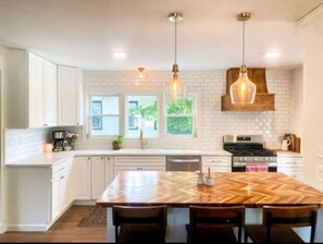 A modern kitchen with white cabinetry, a large wooden island, pendant lighting, and a brick backsplash.