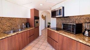 Une cuisine de taille réduite dotée de plans de travail en granit, d’appareils électroménagers en acier inoxydable et d’armoires en bois.