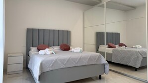 A modern bedroom with a large mirror, a grey bed with white bedding, and a small bedside table. - Modern apartment in the center 700 meters from the shores of Lake Garda (Desenzano del Garda)