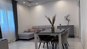 A modern living room with a glass-top dining table, grey sofa, and a radiator. - Modern apartment in the center 700 meters from the shores of Lake Garda (Desenzano del Garda)