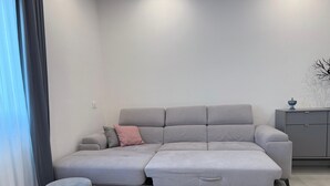 A modern living room with a grey sectional sofa, a small ottoman, a grey rug, and a grey cabinet with a decorative item on top. - Modern apartment in the center 700 meters from the shores of Lake Garda (Desenzano del Garda)