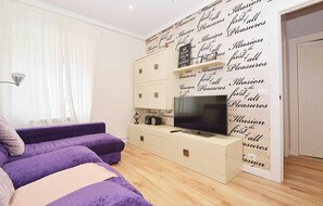 A modern living room with a purple sofa, a flat-screen TV, and a white cabinet with drawers.