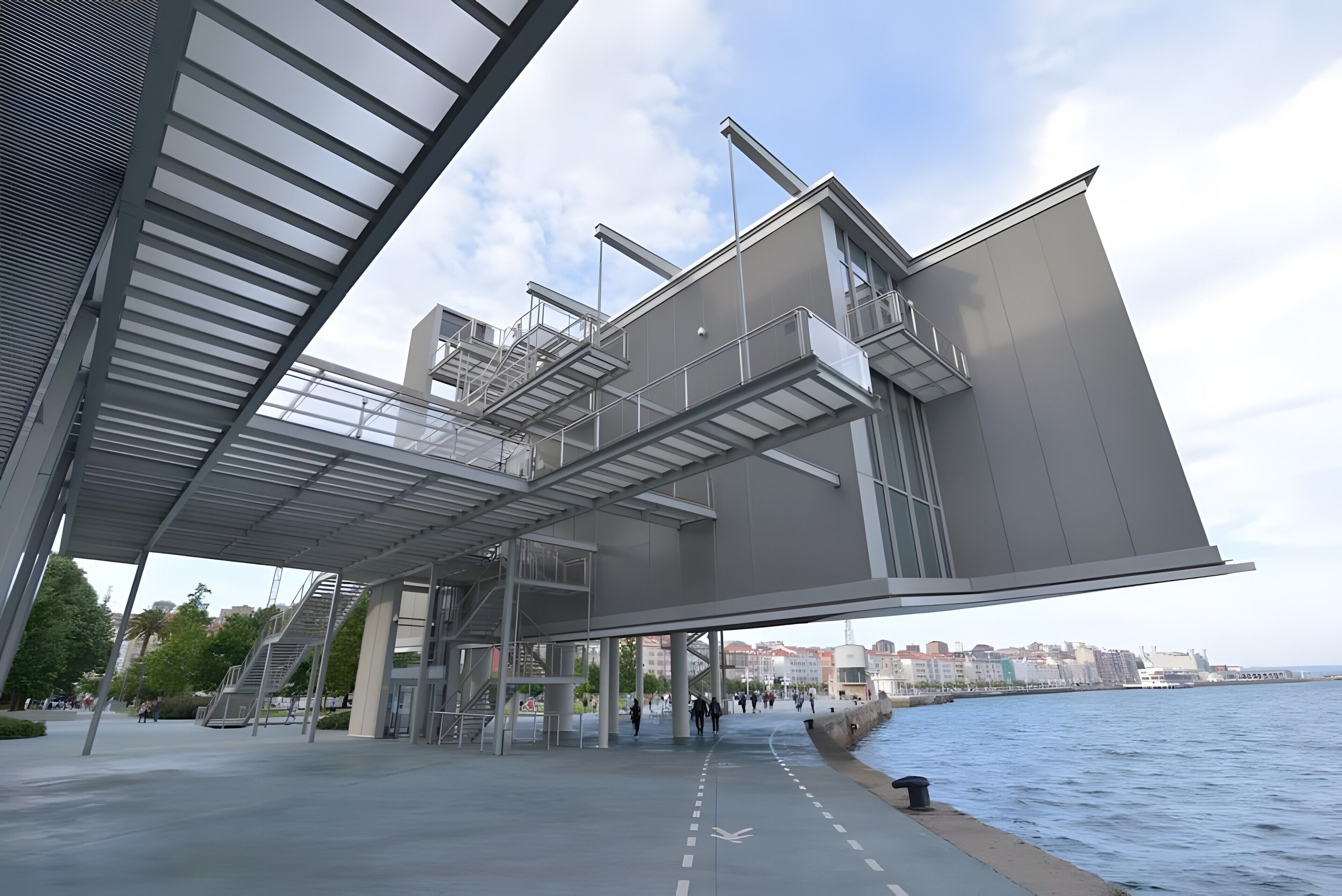 A modern architectural structure with a glass facade, metal framework, and a waterfront view.