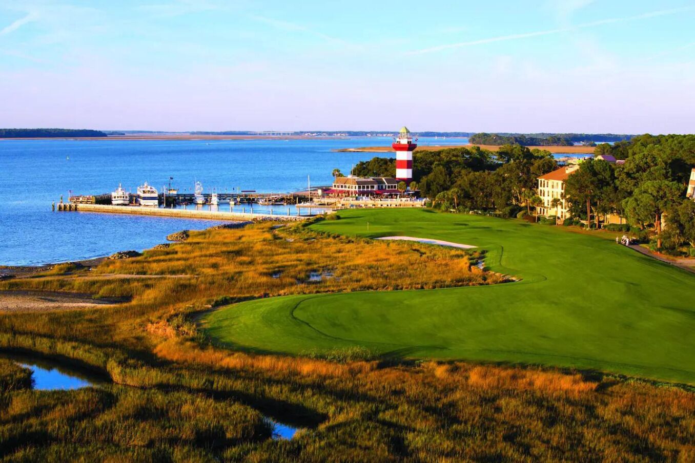 A coastal golf course with a lighthouse, water, and buildings.