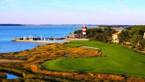 Un campo de golf costero con un faro, agua y edificios.