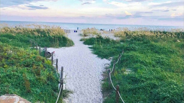 Un sendero arenoso que conduce a una playa con dunas cubiertas de hierba a ambos lados.