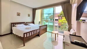 Habitación de hotel con una cama grande, una mesita, televisor y balcón con vistas al barrio.