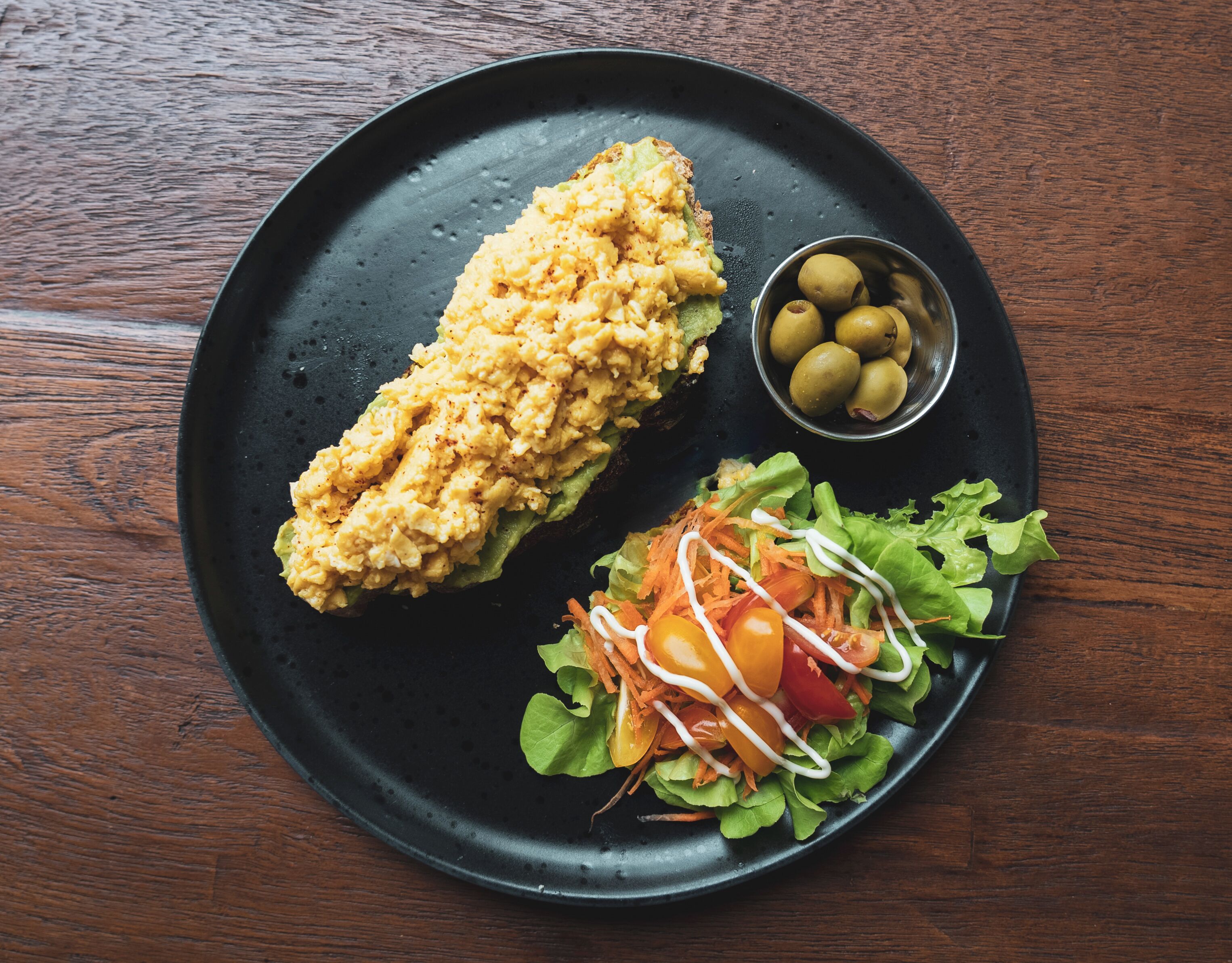 A black plate with a fried item, a salad, and a small bowl of olives.