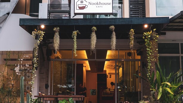 Un edificio con un letrero que indica Nookhouse Cafe, que presenta una escalera que lleva a la entrada, plantas en macetas y una pizarra con el menú en el exterior.