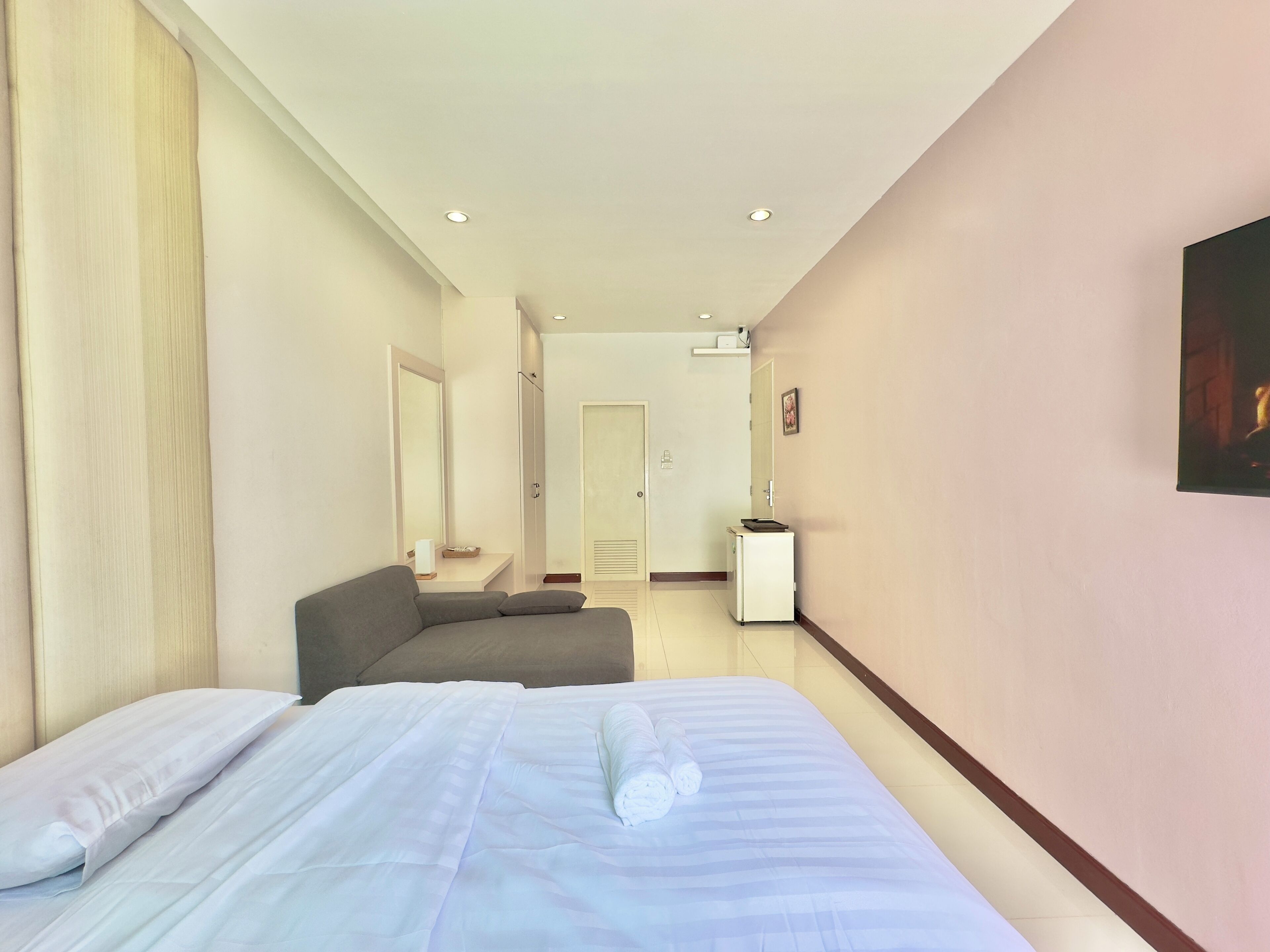 A hotel room with a bed, a sofa, a small table, a mirror, and a door leading to another room.