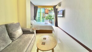 Habitación de hotel con sofá, cama, televisión y balcón con vistas a zonas verdes.