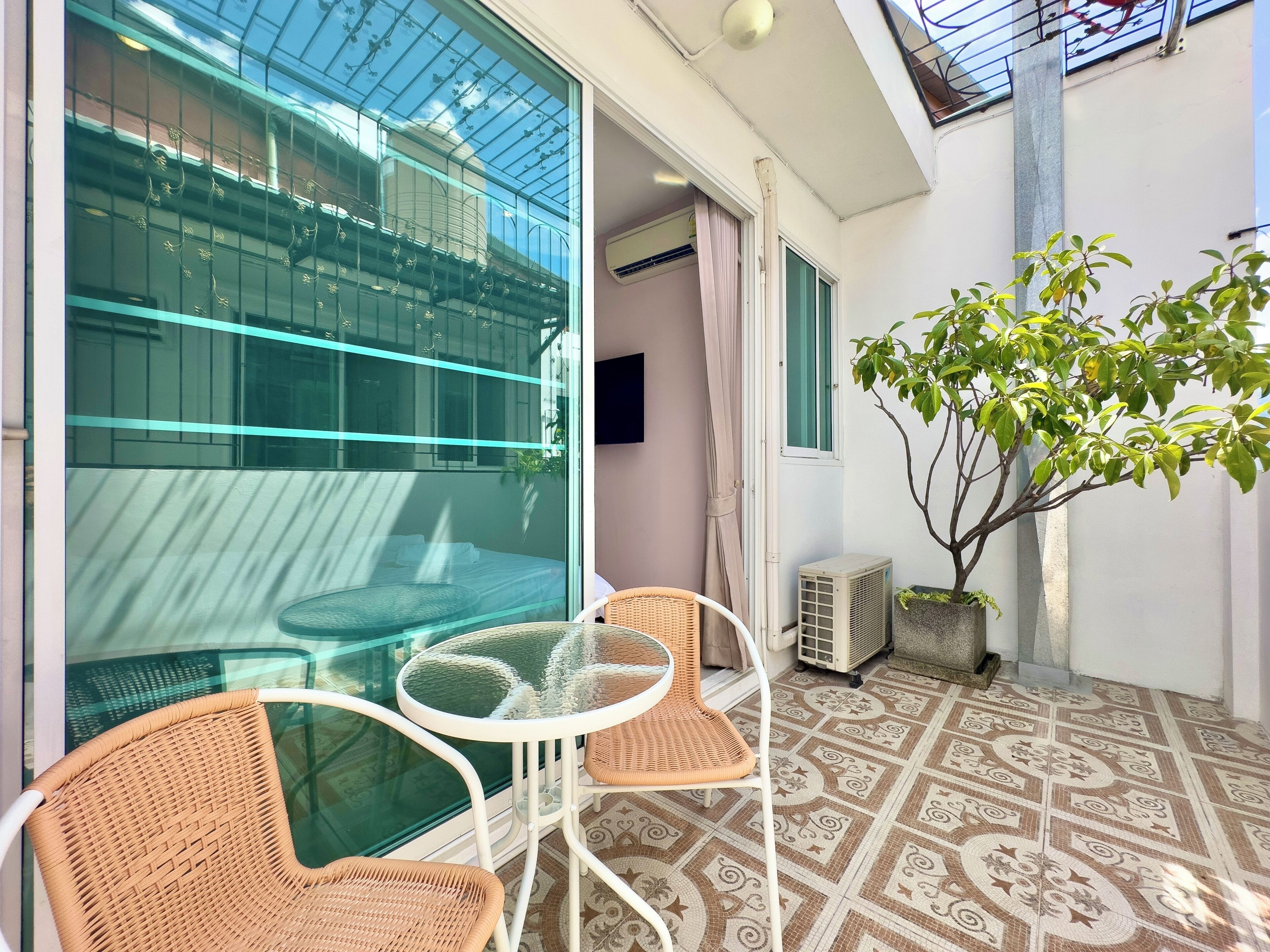 A balcony with wicker chairs and a glass table, a potted plant, and a patterned floor.