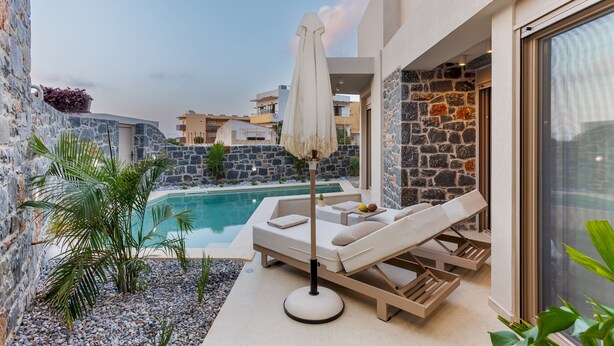 A modern outdoor pool area with lounge chairs and a sun umbrella, surrounded by stone walls and plants.