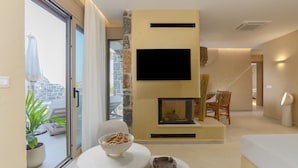 A modern living room with a fireplace, a flat-screen TV mounted on the wall, and a dining area with a bowl of snacks.