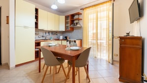 Un coin repas avec une table et des chaises en bois, une cuisine avec des meubles de couleur claire et un téléviseur fixé au mur.