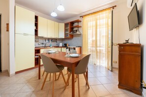 Un coin repas avec une table et des chaises en bois, une cuisine avec des meubles de couleur claire et un téléviseur fixé au mur.