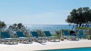 A poolside area with lounge chairs and a view of the sea. - Apartment '4 Personne' with Shared Pool, Wi-Fi and Air Conditioning (Cervione)