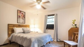 A bedroom with a bed, a ceiling fan, a window with curtains, a desk with a chair, and a painting on the wall. - Private Poconos Family Rancher (Albrightsville)