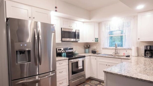 A modern kitchen with stainless steel appliances, white cabinetry, a microwave, and a window with curtains. - Private Poconos Family Rancher (Albrightsville)