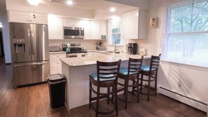 A modern kitchen with stainless steel appliances, a central island with bar stools, and a large window providing natural light. - Private Poconos Family Rancher (Albrightsville)