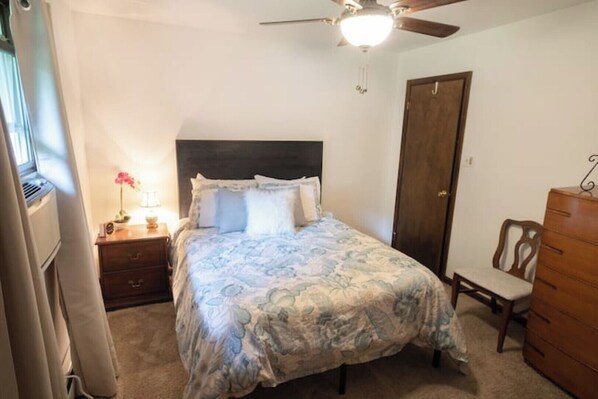 Une chambre à coucher comprenant un lit, une table de chevet, une commode, une chaise et un ventilateur de plafond.