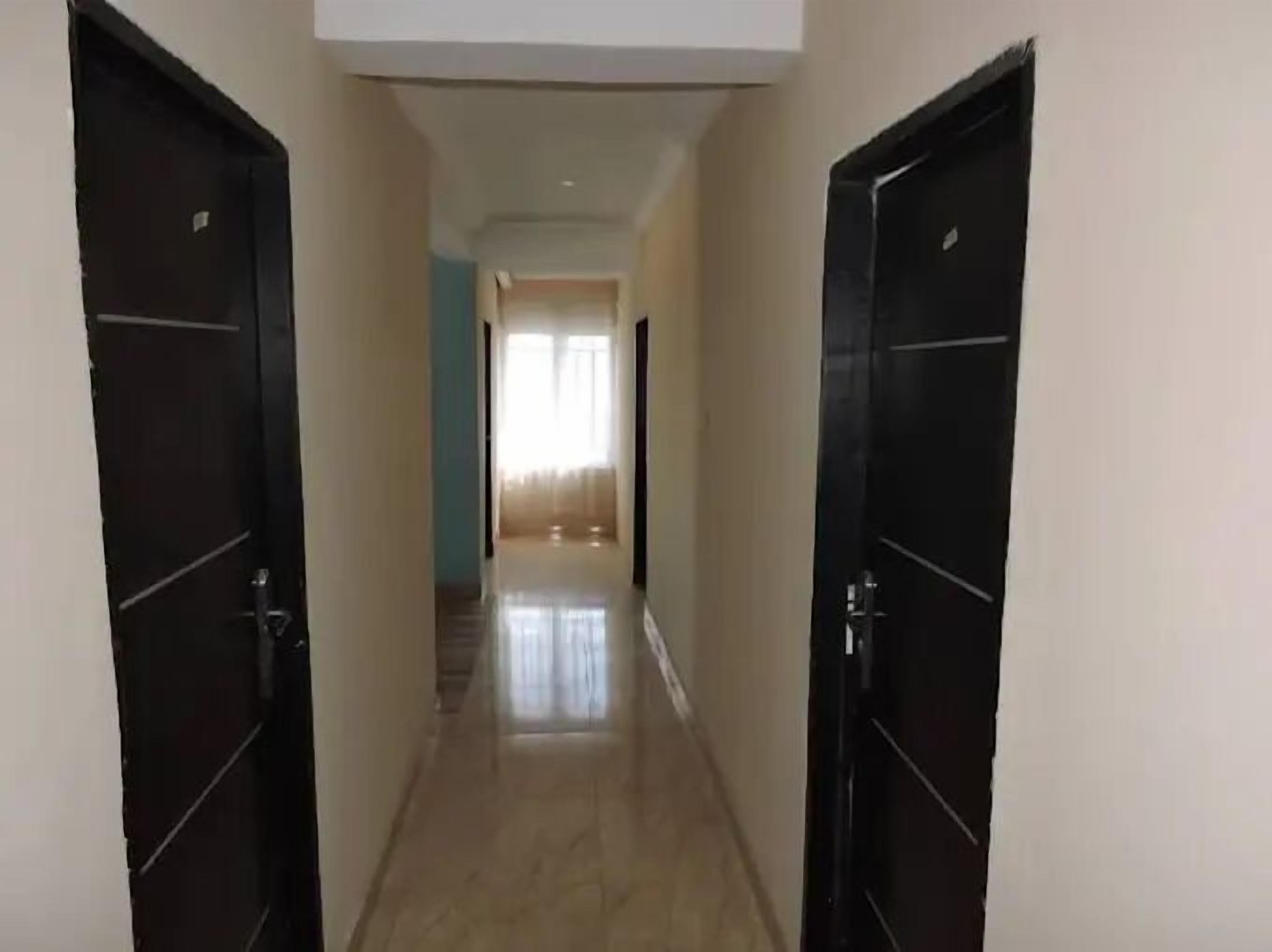 A corridor with two black doors on either side, leading to a room with a window and a view of the outside.