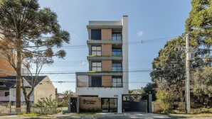 A multi-story building with a flat facade, a gated entrance, and a sign indicating it is a condominium. - Apto próx. Ópera de Arame c\/ Garagem PLA0408 (Curitiba)