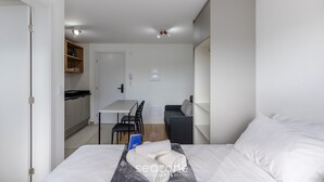A modern hotel room with a bed, a desk, and a dining area. - Apto próx. Ópera de Arame c\/ Garagem PLA0408 (Curitiba)