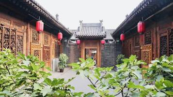 A traditional courtyard with wooden buildings, red lanterns, and lush greenery.