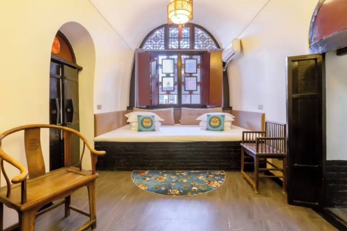 Um quarto com uma cama, uma cadeira de madeira, uma mesinha e um tapete decorativo.