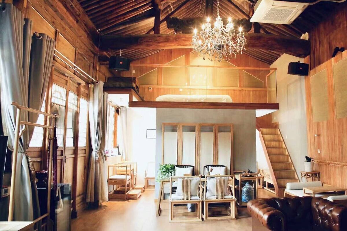 Um quarto amplo em estilo loft, com teto alto, vigas de madeira, lustre e cama em mezzanine.