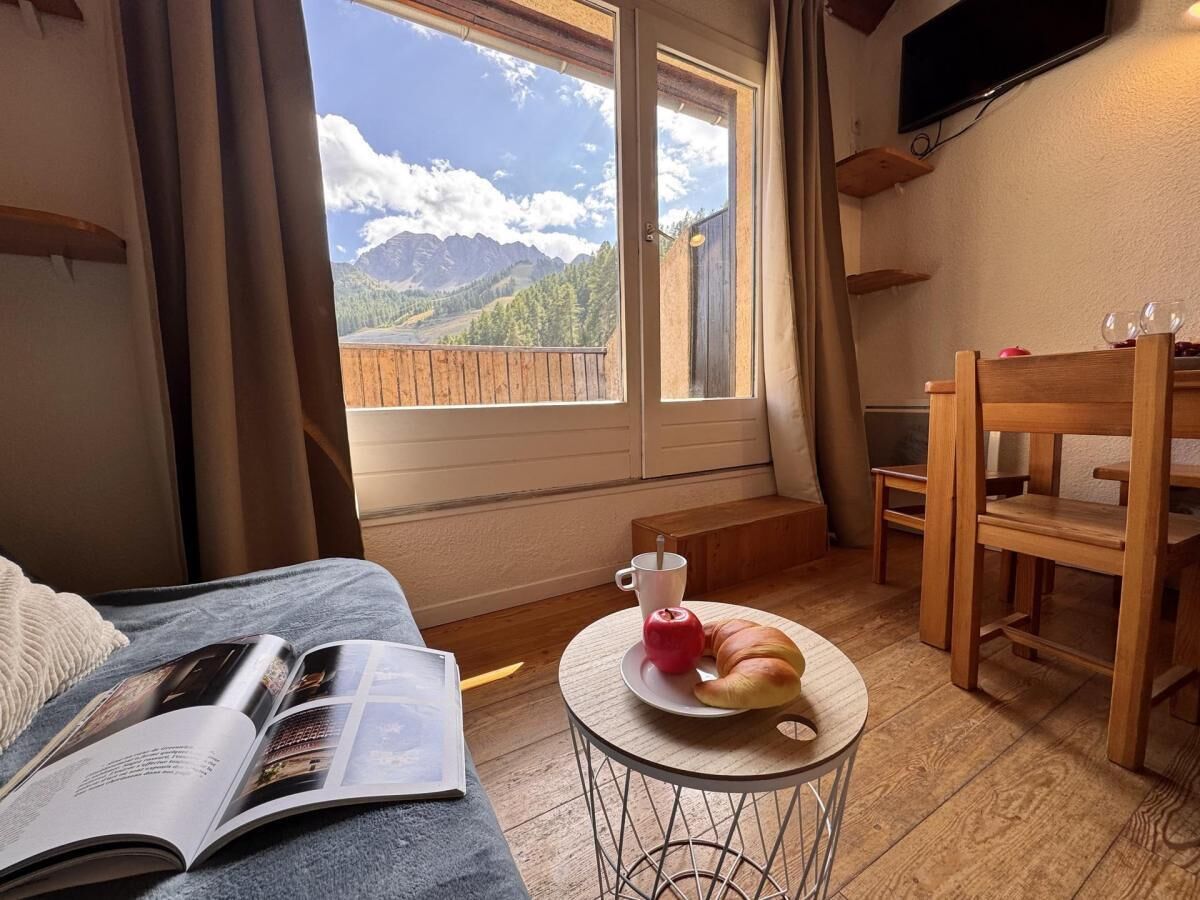 Ein gemütliches Zimmer mit einem Bett, einem kleinen Tisch mit einem Croissant und einer Tasse sowie Blick auf Berge durch ein Fenster.