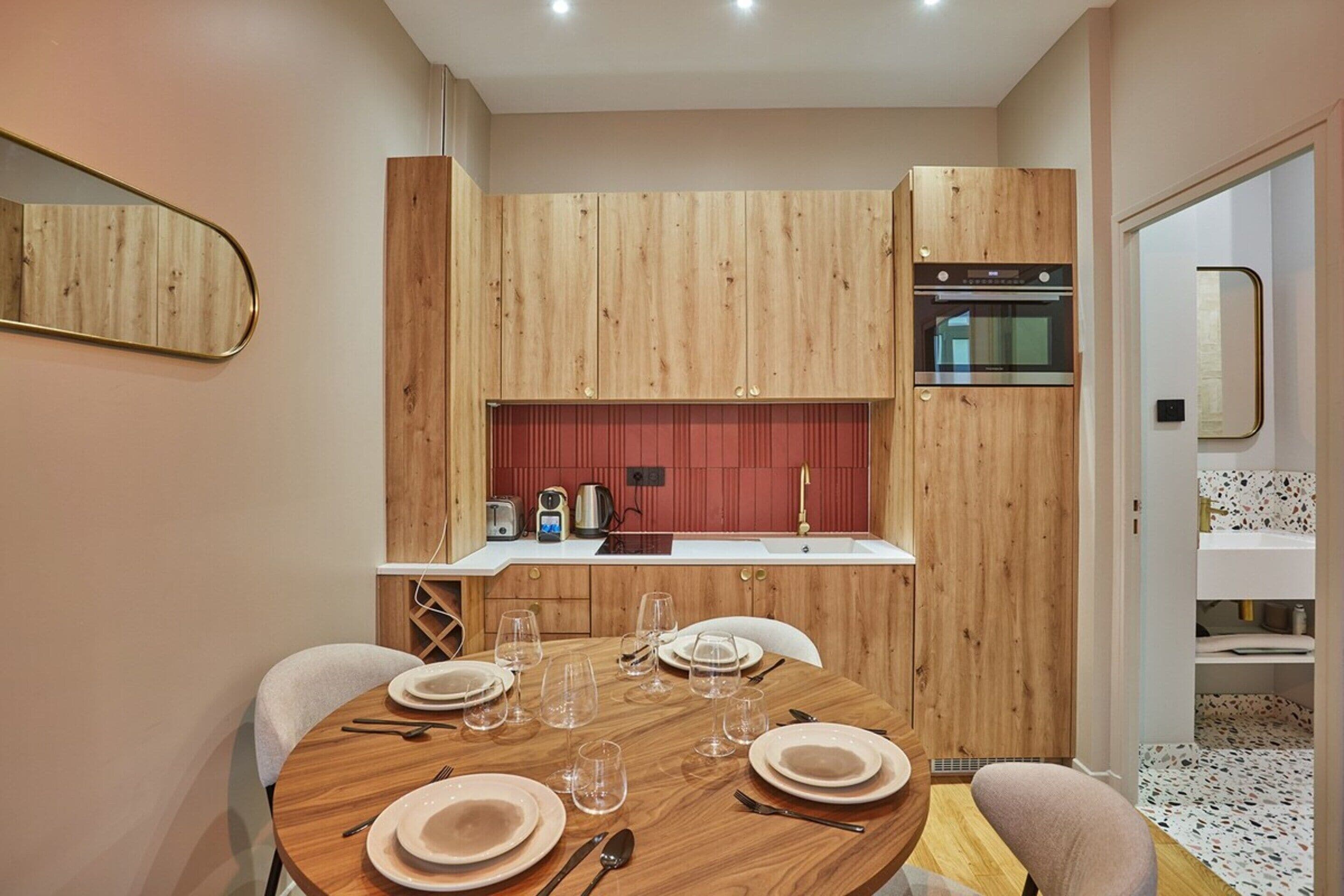 A modern kitchen with wooden cabinets, a built-in oven, and a dining area with a round table set for four.