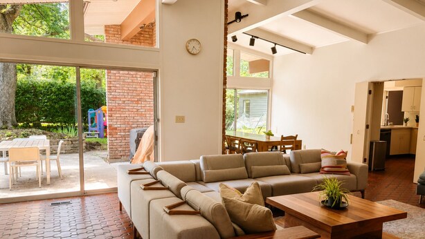 Una sala de estar moderna con un sofá modular, una mesa de centro de madera y un amplio ventanal corredera que da a un patio exterior.