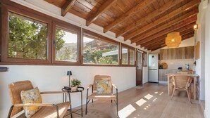 A spacious room with large windows, a kitchen area, and wicker furniture.