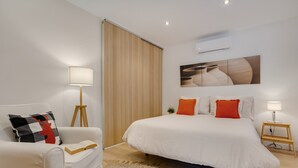 A modern hotel room with a bed, a sofa, a lamp, and a painting on the wall.