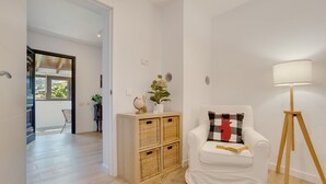 A room with a white sofa, a lamp, a small table with a globe and a plant, and a wicker storage unit.