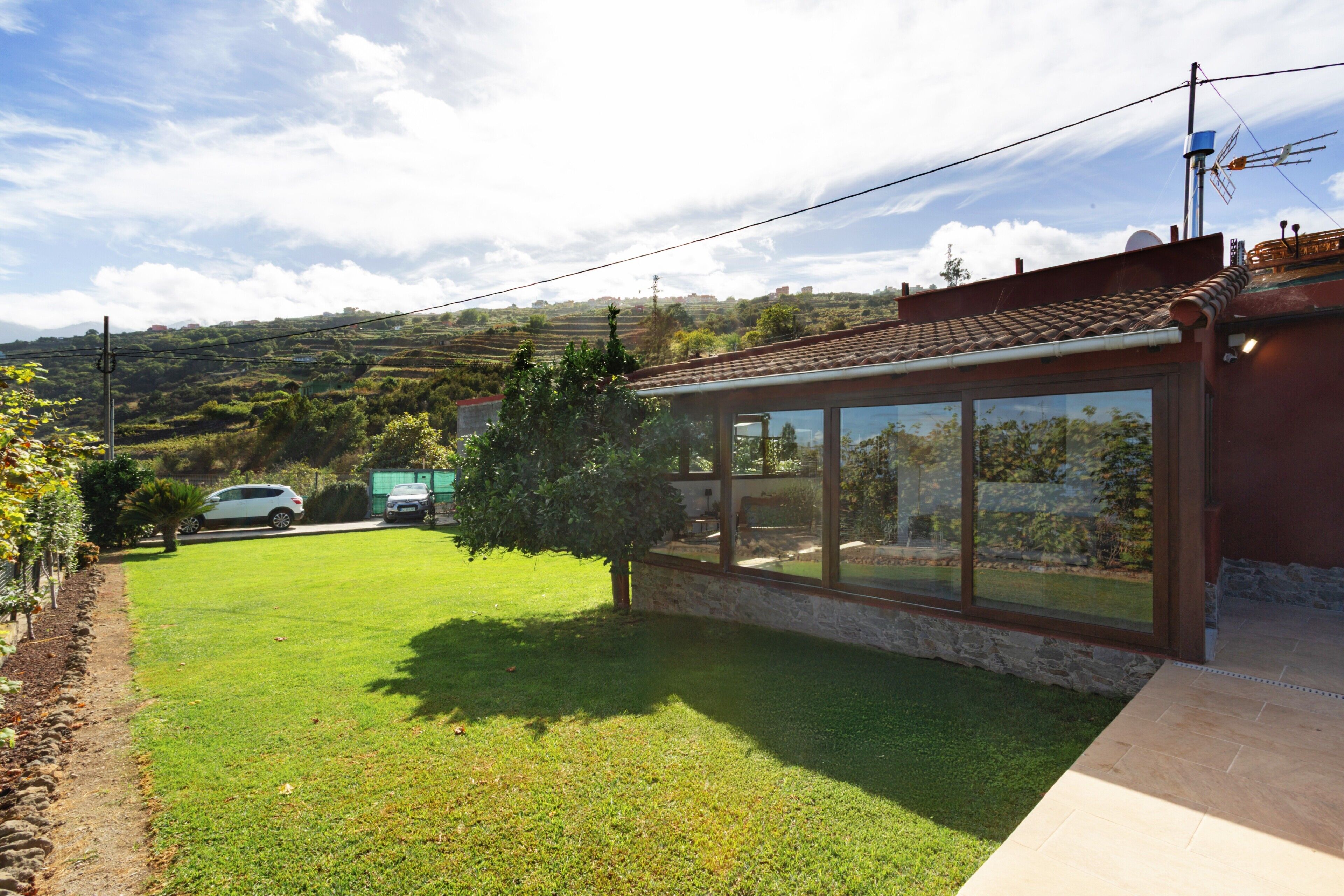 A modern house with a large glass window, a well-maintained lawn, and a view of the countryside.