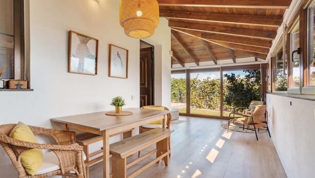 A spacious room with a wooden table, wicker chairs, and a large window offering a view of the outdoors.