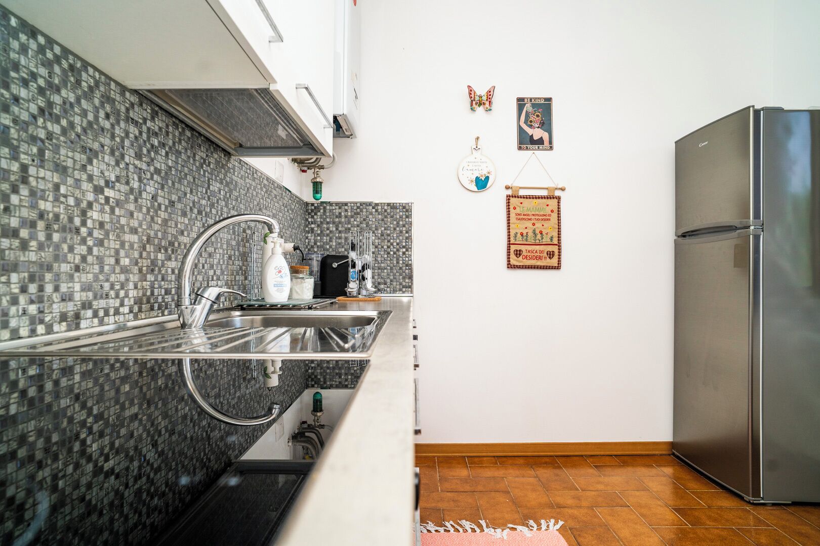 A modern kitchen with a stainless steel refrigerator, a sink with a faucet, and a tiled backsplash.