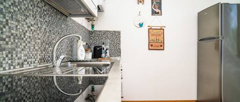 A modern kitchen with a stainless steel refrigerator, a sink with a faucet, and a tiled backsplash.