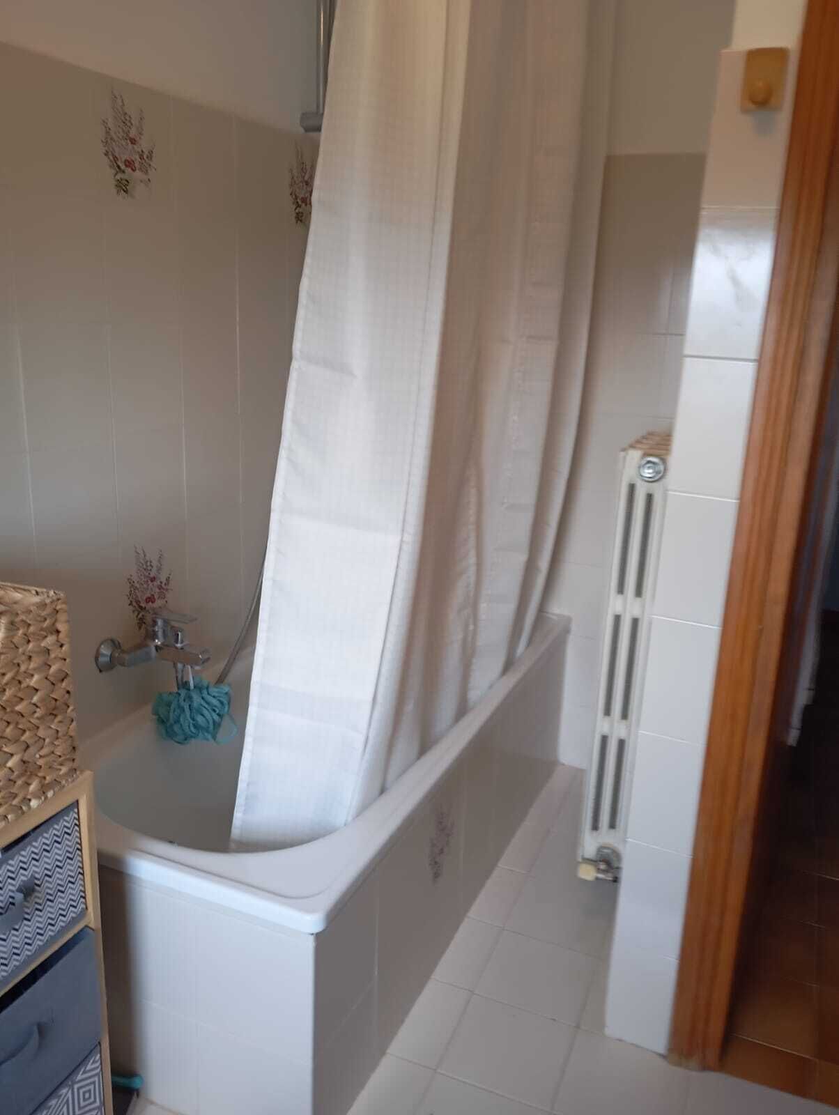 Een badkamer met een bad, douchegordijn, handdoekradiator en handdoekhouder.