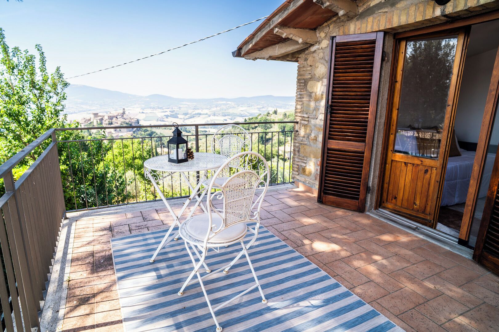 A balcony with a table and chairs, a view of the countryside, and a wooden door.