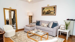 A living room with a grey sofa, a white armchair, a coffee table, a lamp, a framed picture, and a vase with flowers. - Charming Tuscany style home with AC and heater in beautiful Umbria. (Umbria)