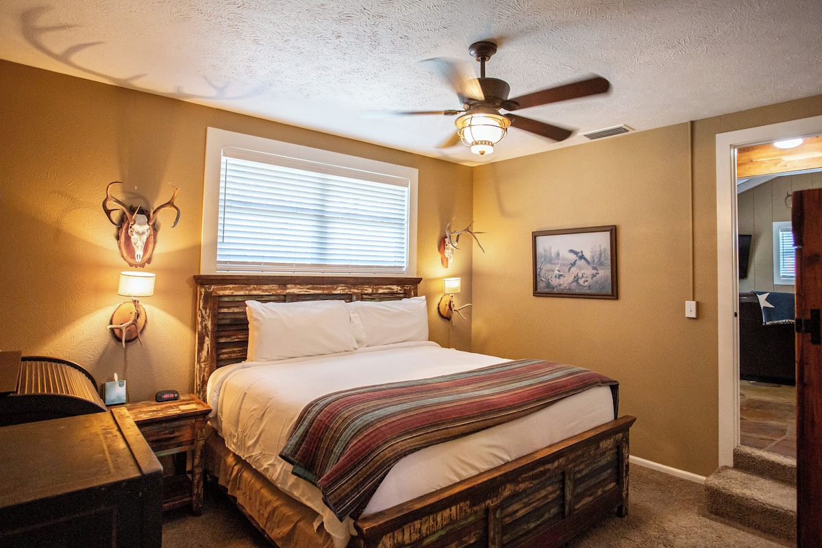 Une chambre à coucher avec un lit en bois, un ventilateur de plafond, une fenêtre avec des stores et des lampes fixées au mur.