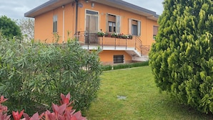 A two-story house with a balcony, surrounded by greenery and a well-maintained lawn. - Casa Giorgia welcomes you to the greenery of the Delta with its relaxing quietness (Rosolina)