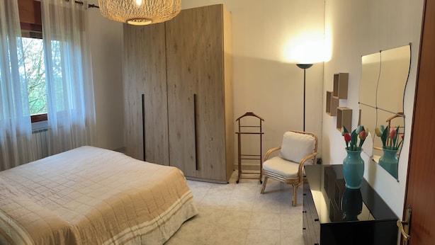 A bedroom with a bed, a wardrobe, a chair, a dresser, a mirror, and a hanging light fixture. - Casa Giorgia welcomes you to the greenery of the Delta with its relaxing quietness (Rosolina)
